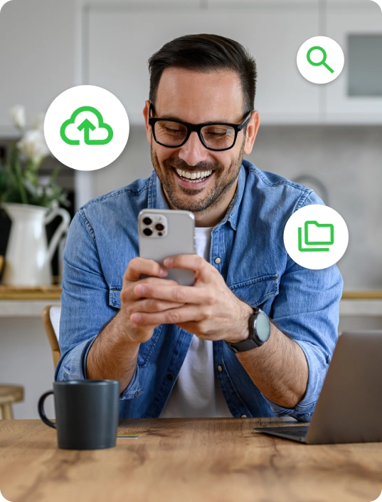 A man sits at a table and looks at his phone. There are three icons floating around him.